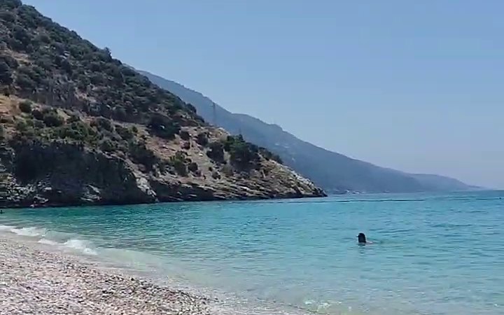 Fethiye yakınında dik, yeşil bir dağın altında turkuaz deniz ve beyaz çakıllı bir plaj.